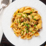 Overhead chicken thigh and chorizo sausage pasta served with garlic bread.