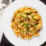 Overhead chicken thigh and chorizo sausage pasta served with garlic bread.