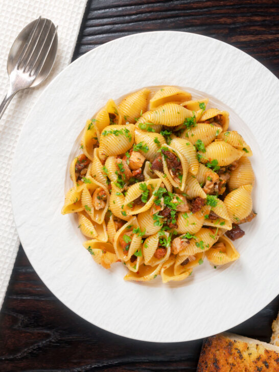 Overhead chicken thigh and chorizo sausage pasta served with garlic bread.