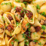 Close-up overhead chicken thigh and chorizo sausage pasta featuring a title overlay.