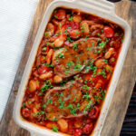 Overhead pork chop casserole with cherry tomatoes and beans in a casserole dish.