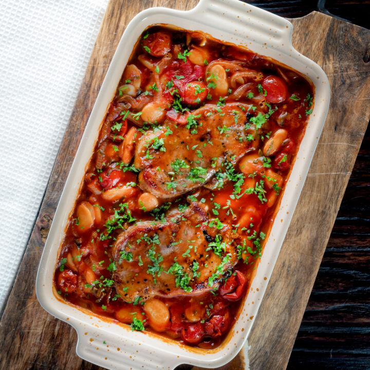 Boneless pork chop casserole with tomatoes and butter beans in a casserole dish.