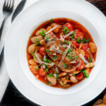 Overhead pork chop casserole with cherry tomatoes and beans served with bread.
