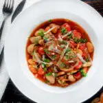 Overhead pork chop casserole with cherry tomatoes and beans served with bread featuring a title overlay.