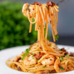 Prawn and chorizo pasta with fresh parsley being picked up with a fork.