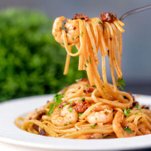 Close-up prawn and chorizo pasta being picked up with a fork.