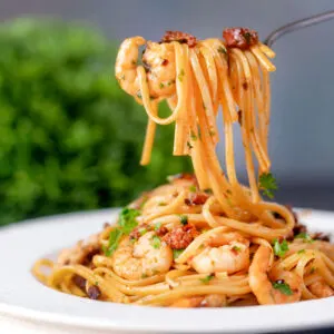 Close-up prawn and chorizo pasta being picked up with a fork.