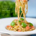Pasta pesto alla trapanese fresh tomato and basil being picked up with a fork featuring a title overlay.