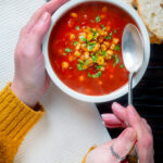 Overhead spicy vegan sweetcorn soup with tomato and chipotle being eaten.