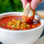 Bread being dipped into a spicy vegan sweetcorn soup.