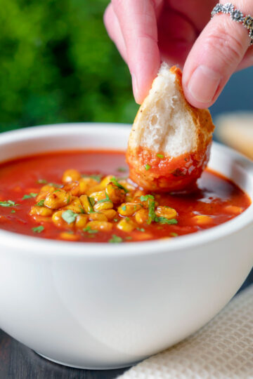 Bread being dipped into a spicy vegan sweetcorn soup.