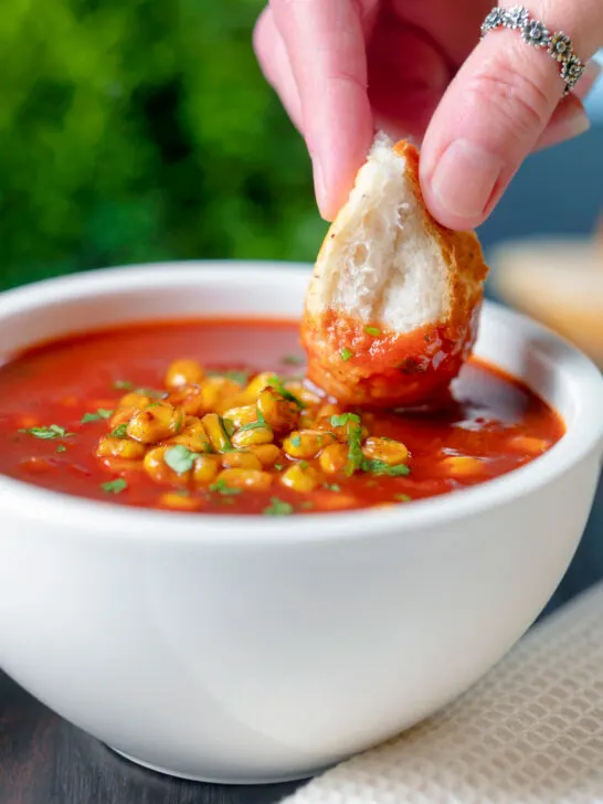 Bread being dipped into a spicy vegan sweetcorn soup.