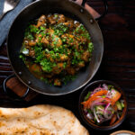 Overhead Tamil black pepper chicken curry, aka Chettinad chicken with naan and salad.