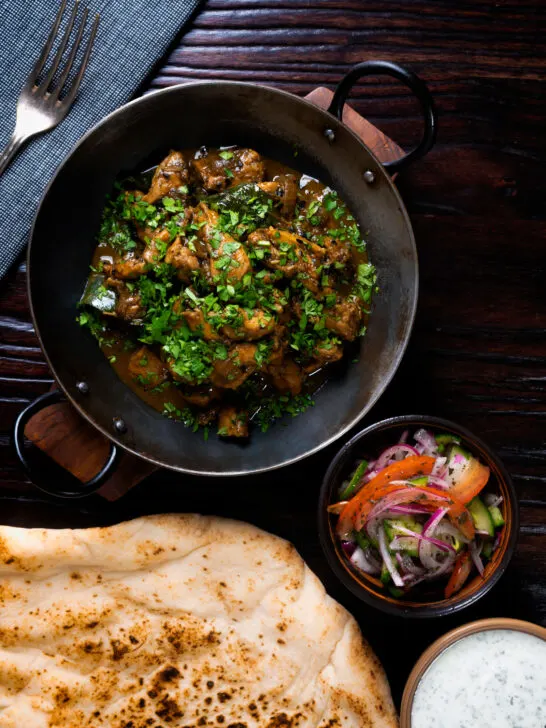 Overhead Tamil black pepper chicken curry, aka Chettinad chicken with naan and salad.