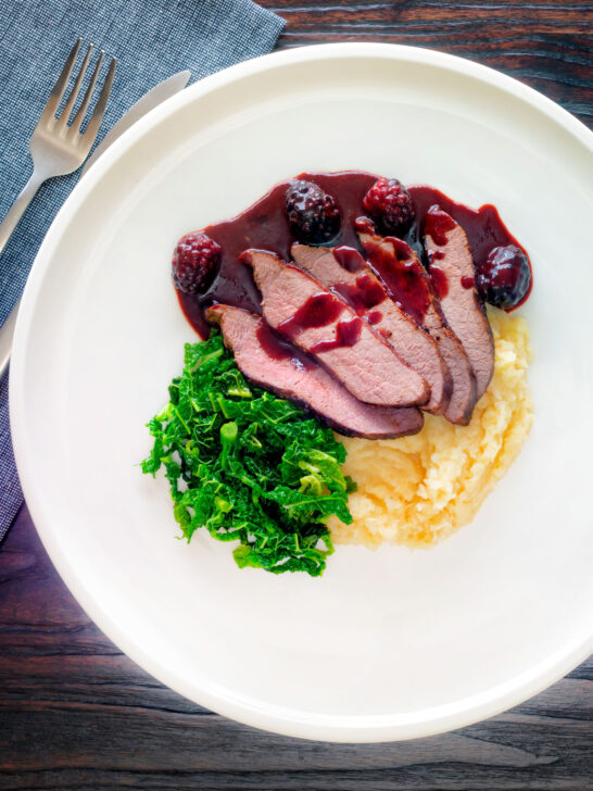 Overhead wild boar haunch steak with blackberry sauce, cabbage and mashed potato.