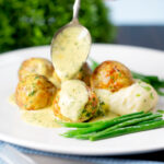 Creamy honey mustard sauce being poured over minced chicken meatballs.