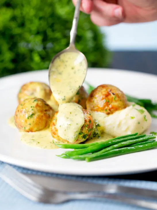 Creamy honey mustard sauce being poured over minced chicken meatballs.