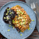 Overhead sticky hoisin duck leg served with a cucumber and soba noodle salad featuring a title overlay.