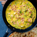 Chicken pasanda yoghurt, coriander and almond curry served in a cooking pan with a naan bread featuring a title overlay.