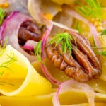 Close-up fennel and orange pappardelle with red onions and pecan nuts.