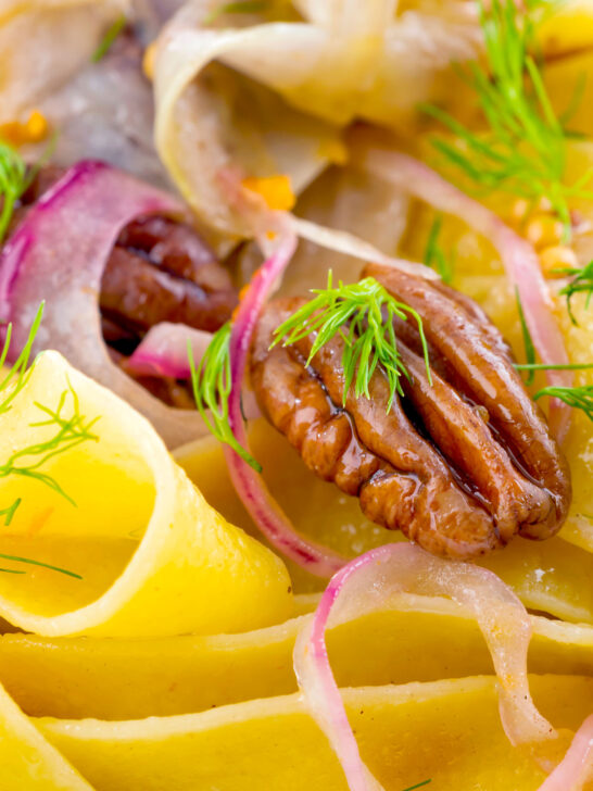 Close-up fennel and orange pappardelle with red onions and pecan nuts.