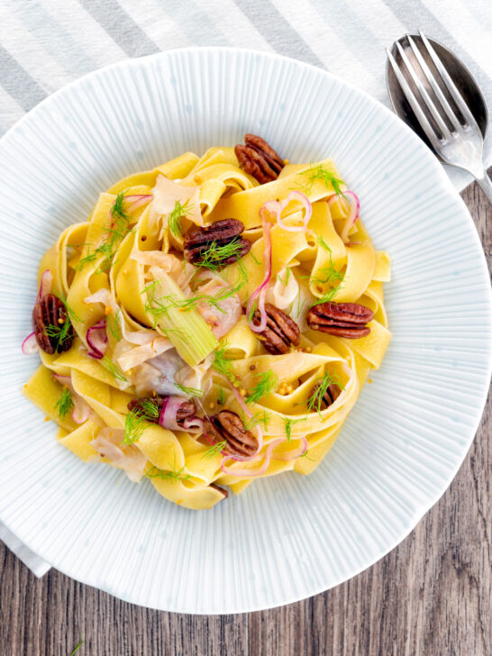 Overhead fennel and orange pasta with red onions and pecan nuts.