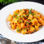 Red pesto halloumi pasta with mezzi rigatoni and fresh basil featuring a title overlay.