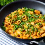 Red pesto halloumi pasta with mezzi rigatoni and fresh basil in a pan.