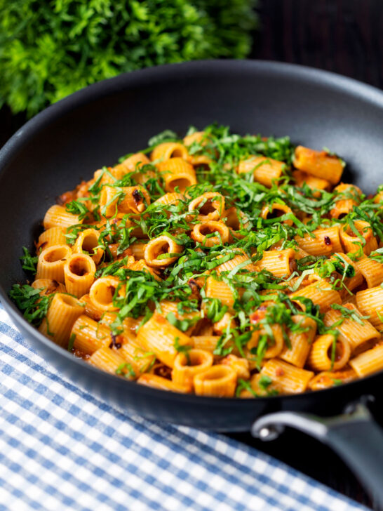 Red pesto halloumi pasta with mezzi rigatoni and fresh basil in a pan.