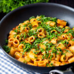 Red pesto halloumi pasta with mezzi rigatoni and fresh basil in a pan featuring a title overlay.