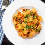 Overhead red pesto halloumi pasta with mezzi rigatoni and fresh basil featuring a title overlay.