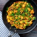 Overhead red pesto halloumi pasta with mezzi rigatoni and fresh basil in a pan.