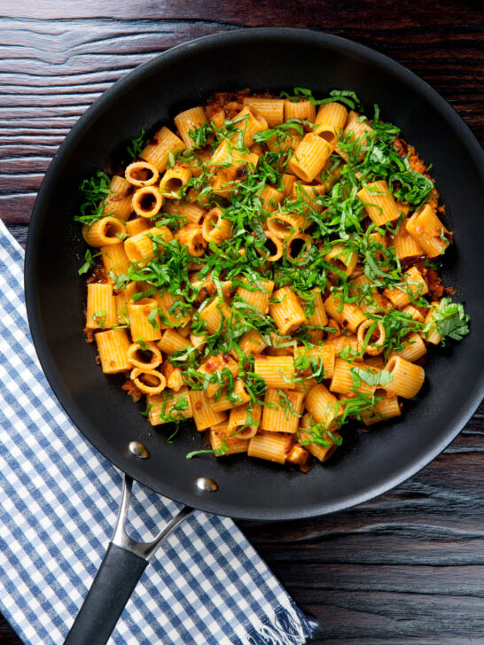 Overhead red pesto halloumi pasta with mezzi rigatoni and fresh basil in a pan.