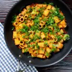 Overhead red pesto halloumi pasta with mezzi rigatoni and fresh basil in a pan featuring a title overlay.