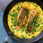 Overhead Indian salmon fillet curry with a yoghurt sauce in the cooking pan.