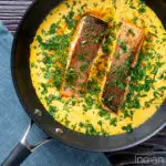 Overhead Indian salmon fillet curry with a yoghurt sauce in the cooking pan featuring a title overlay.