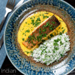 Overhead Indian salmon fillet curry with a yoghurt sauce served with rice featuring a title overlay.