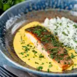 Indian salmon fillet curry with crispy skin in a yoghurt sauce served with rice featuring a title overlay.