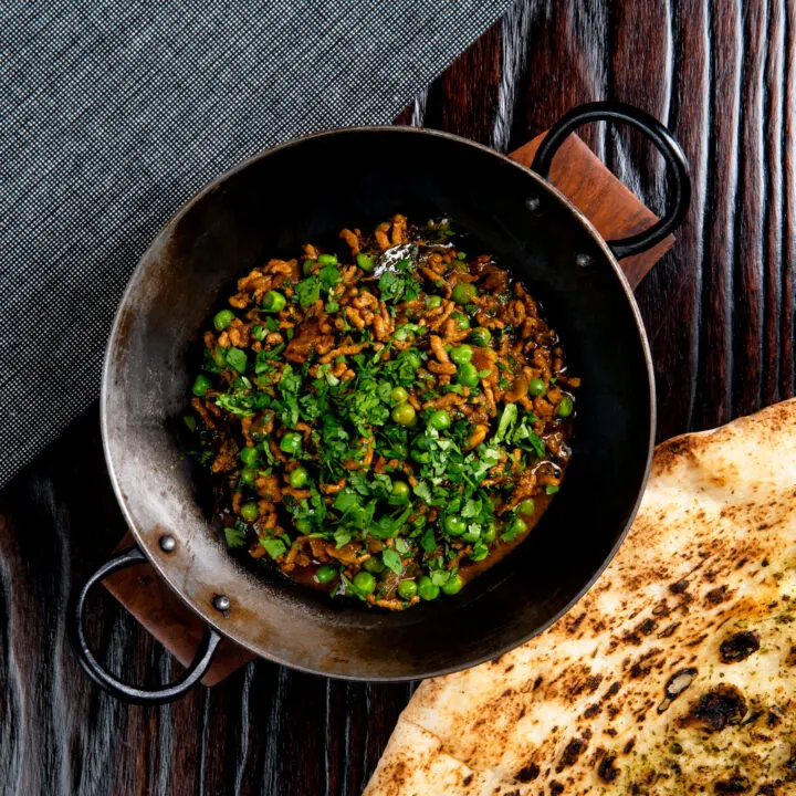 Minced lamb keema matar curry served in a kadai with a naan bread.