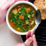 Overhead lentil and bacon soup being eaten with a spoon.