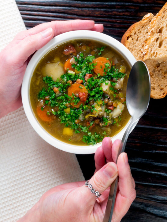 Overhead lentil and bacon soup being eaten with a spoon.