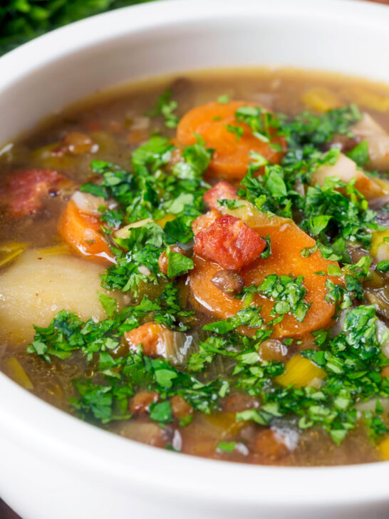 Close-up lentil and bacon soup with root veggies and fresh parsley.