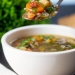 Easy lentil and bacon soup with root veggies and fresh parsley on a spoon.