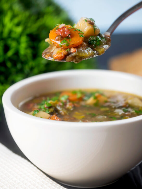 Easy lentil and bacon soup with root veggies and fresh parsley on a spoon.