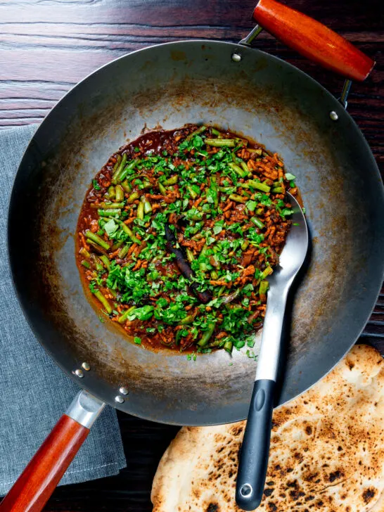 Overhead pork mince curry served in a wok with naan bread.