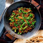 Overhead hot and sour pork mince curry with green beans and naan bread.