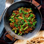 Overhead hot and sour pork mince curry with green beans and naan bread.