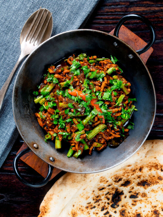 Overhead hot and sour pork mince curry with green beans and naan bread.