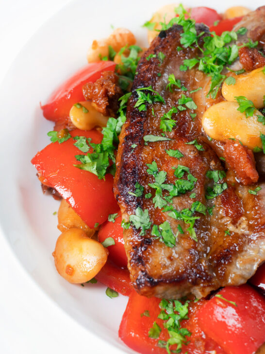 Close-up oven-baked pork loin steaks with chorizo, peppers and beans in a honey glaze.