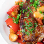 Close-up oven-baked pork loin steaks with chorizo, peppers and beans in a honey glaze featuring a title overlay.